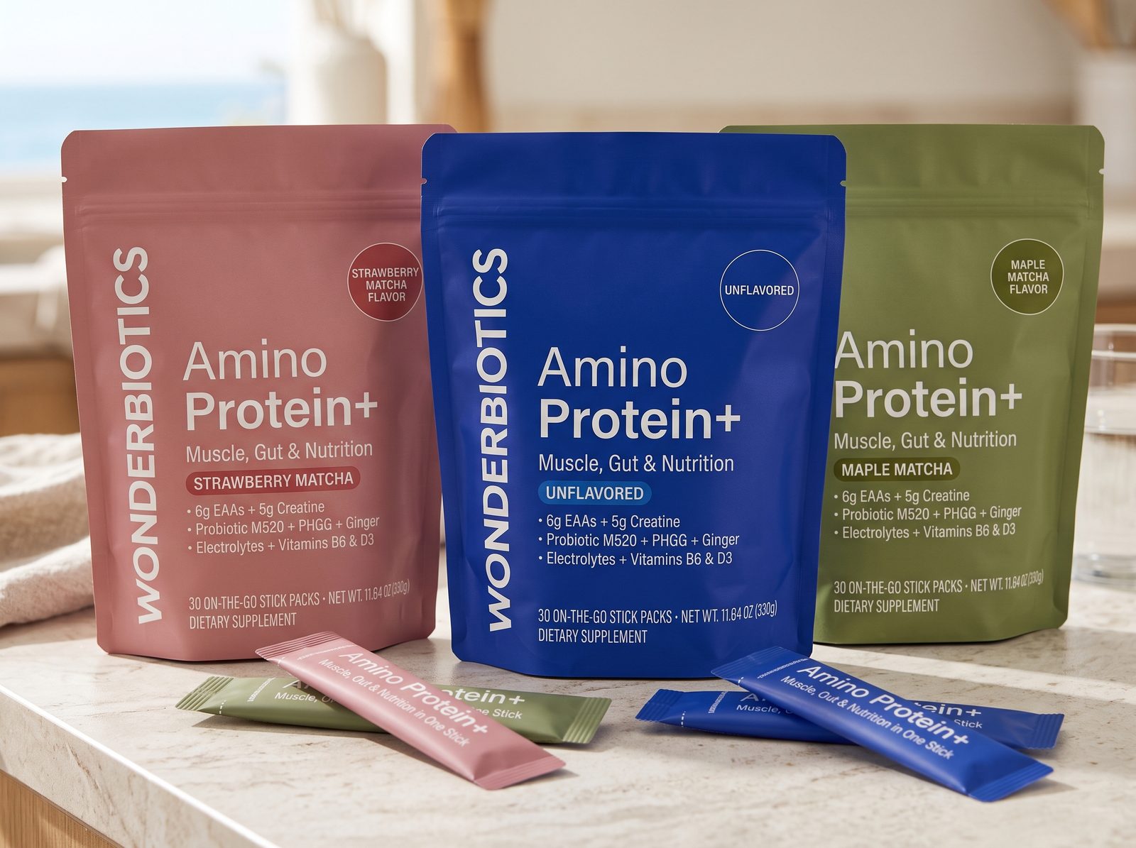 Three Amino Protein+ pouches and stick packs on a coastal stone counter