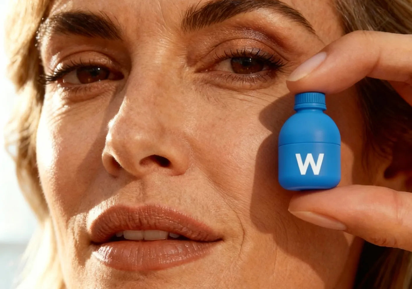 Close-up of a woman holding a blue bottle labeled 'W' near her eye.