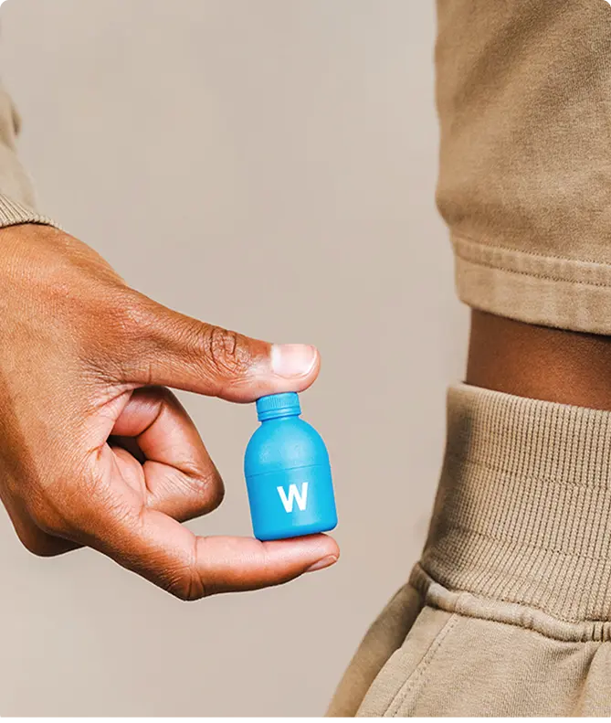 Hand holding a small blue bottle with a “W” mark