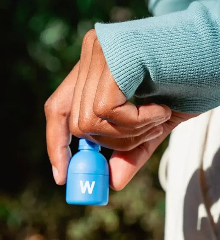 Hand holding a blue water bottle cap with a blurred natural background