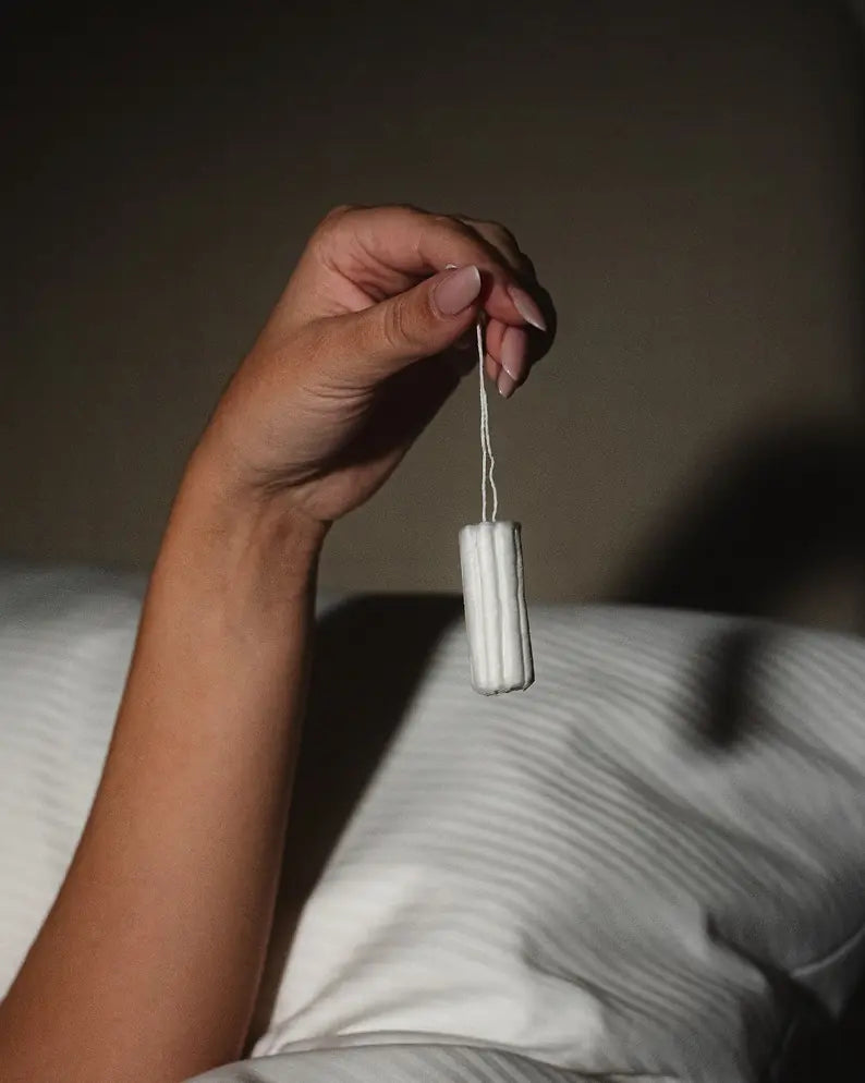 Hand holding a tampon against a neutral background